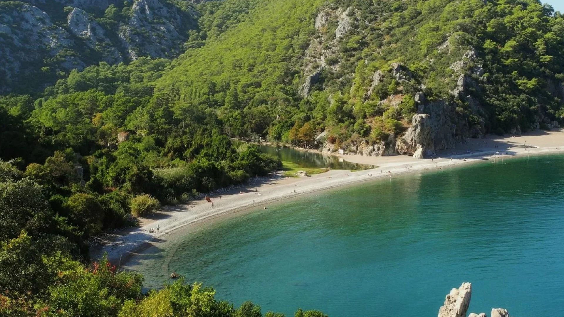 Aerial photo of Olympos Beach showing golden sands meeting turquoise waters, with Lycian ruins hidden in lush greenery - perfect for history and nature lovers.
